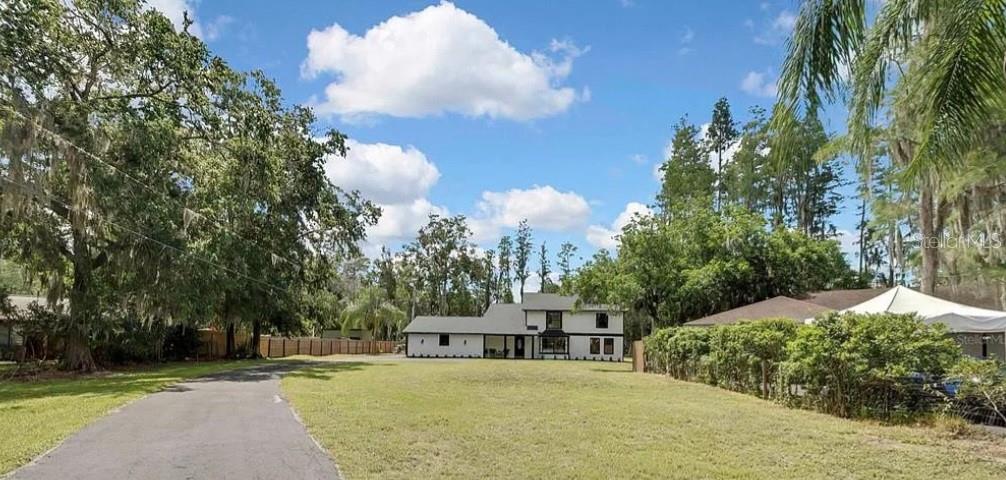 A white two-story house with black trim sits on a large grassy lot with trees — 19003 CEDAR LANE, LUTZ, FL