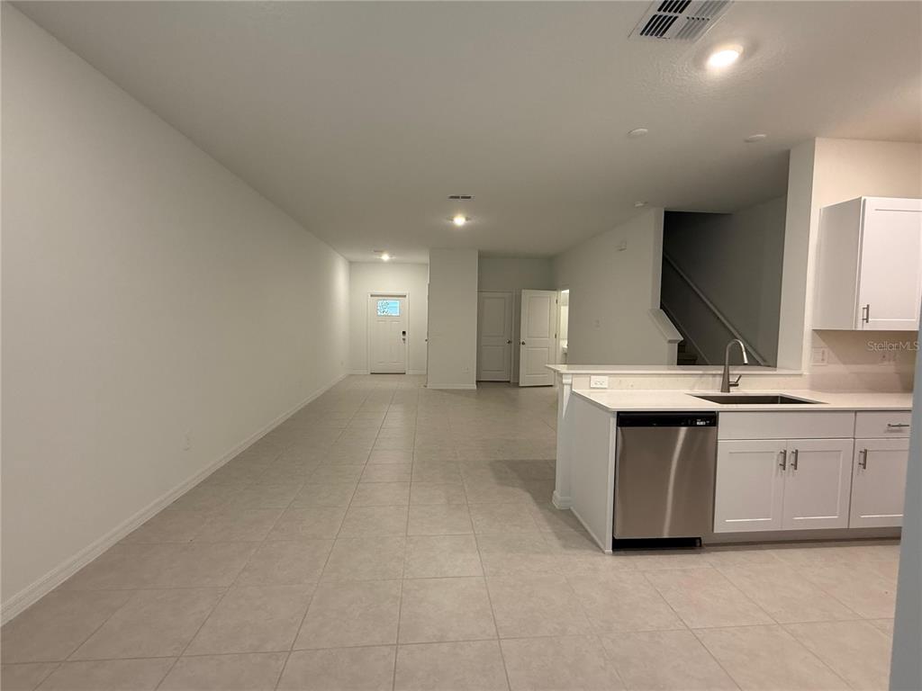 A kitchen with white cabinets and stainless steel appliances overlooks an open-concept living area — 10300 HONEY HAMMOCK WAY, SAN ANTONIO, FL