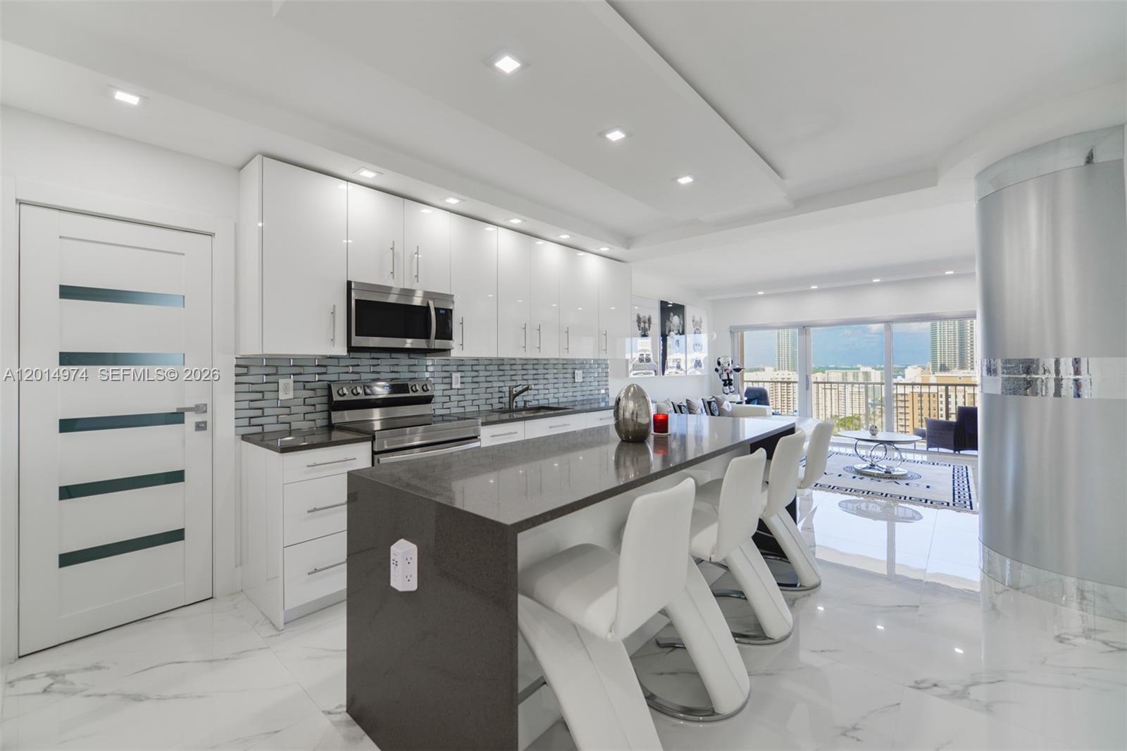 A modern kitchen features white cabinets, a dark gray island, and white marble flooring — 1980 S Ocean Dr, Hallandale Beach FL 33009, HALLANDALE BEACH, FL