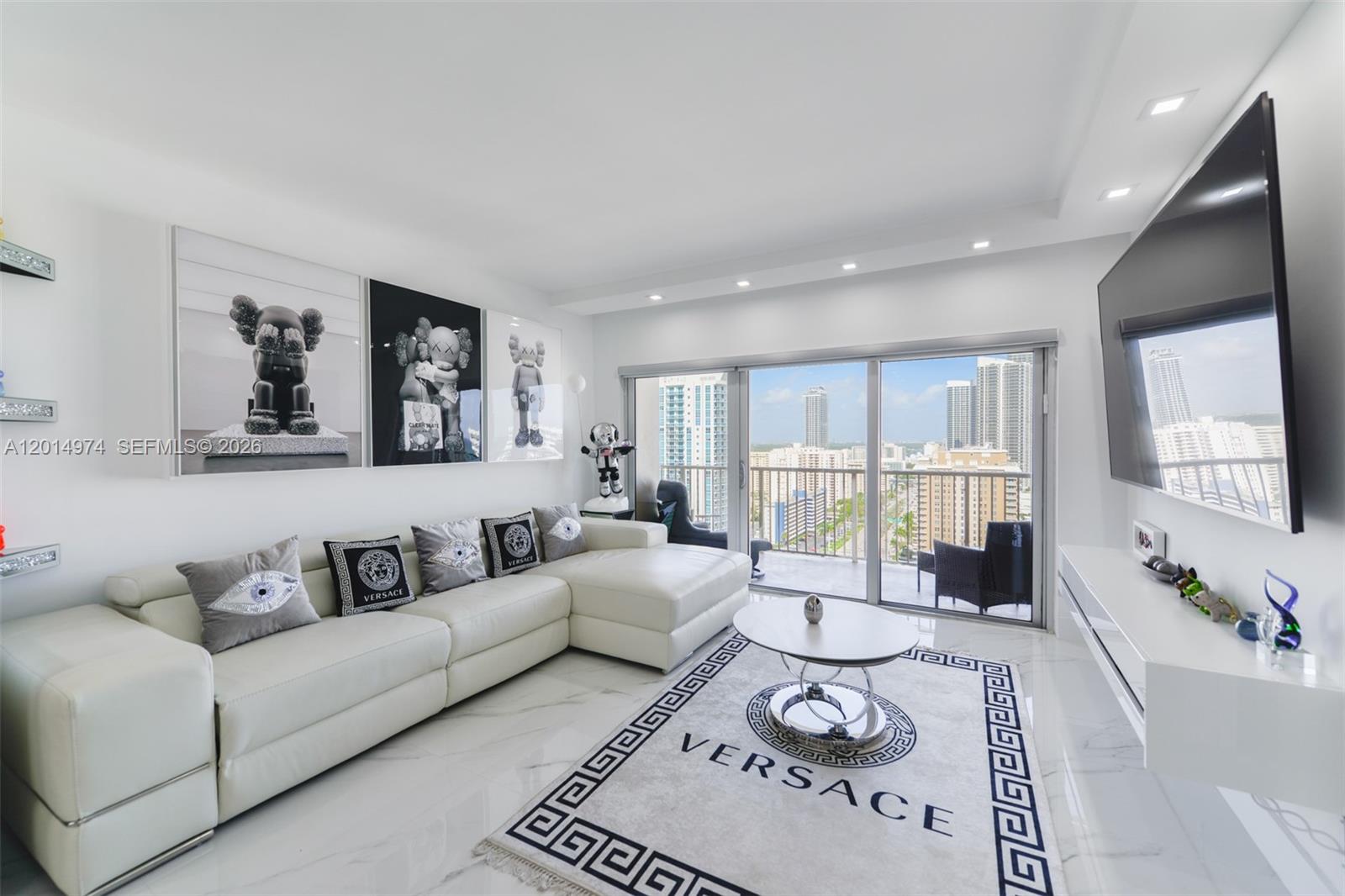 A modern living room features a white sectional sofa, a Versace rug, and a balcony view — 1980 S Ocean Dr, Hallandale Beach FL 33009, HALLANDALE BEACH, FL