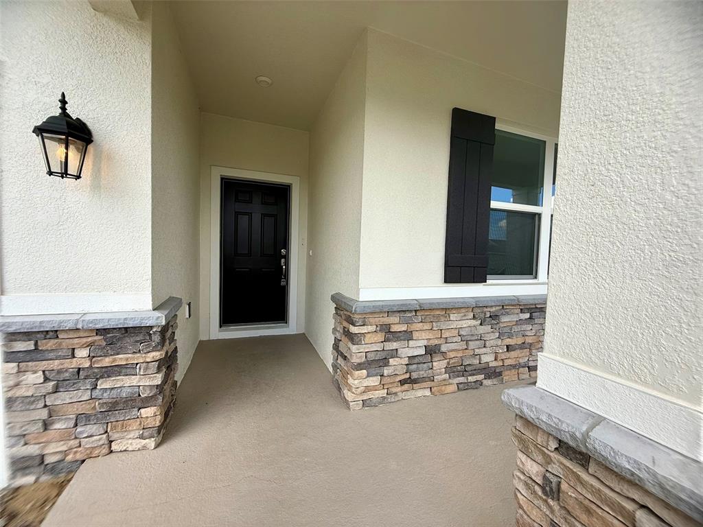 A covered front porch features a black door, stone veneer accents, and a wall lantern — 1306 NORMANDY DRIVE, HAINES CITY, FL