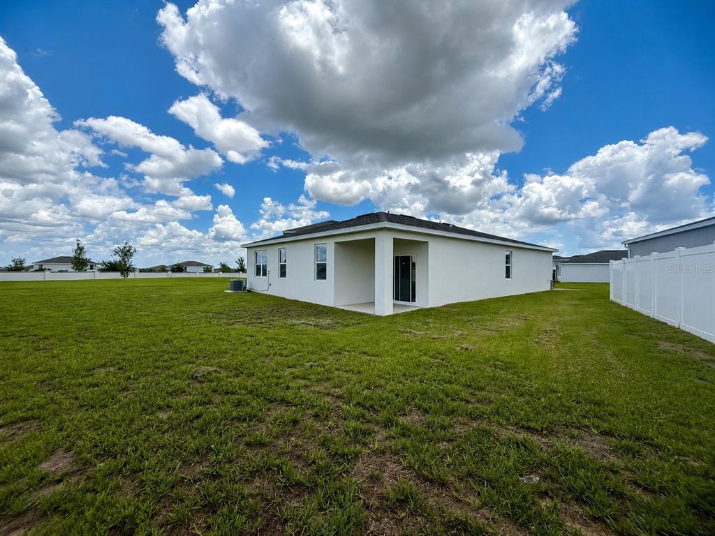 The exterior view shows the back of a white house with a covered patio — 1306 NORMANDY DRIVE, HAINES CITY, FL