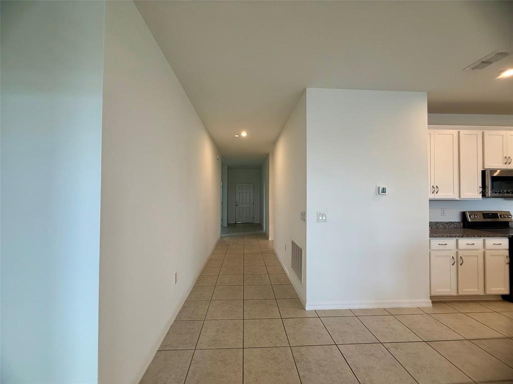 A hallway with tile flooring leads to a closed door, adjacent to a kitchen area — 1306 NORMANDY DRIVE, HAINES CITY, FL