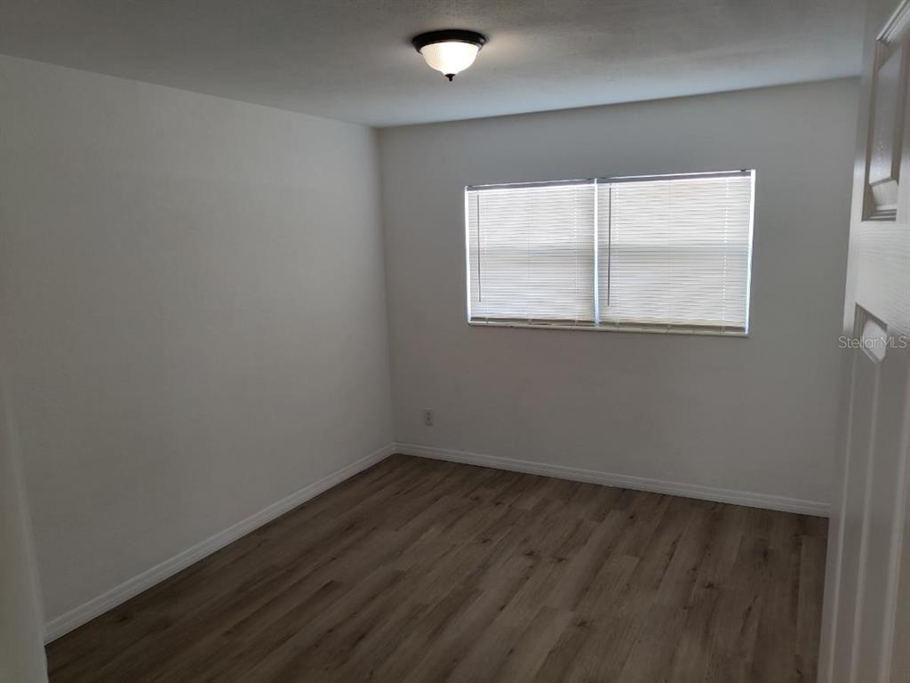 An empty bedroom features white walls, a single window with blinds, and wood-look flooring — 245 - 247 38TH AVENUE SE, ST PETERSBURG, FL