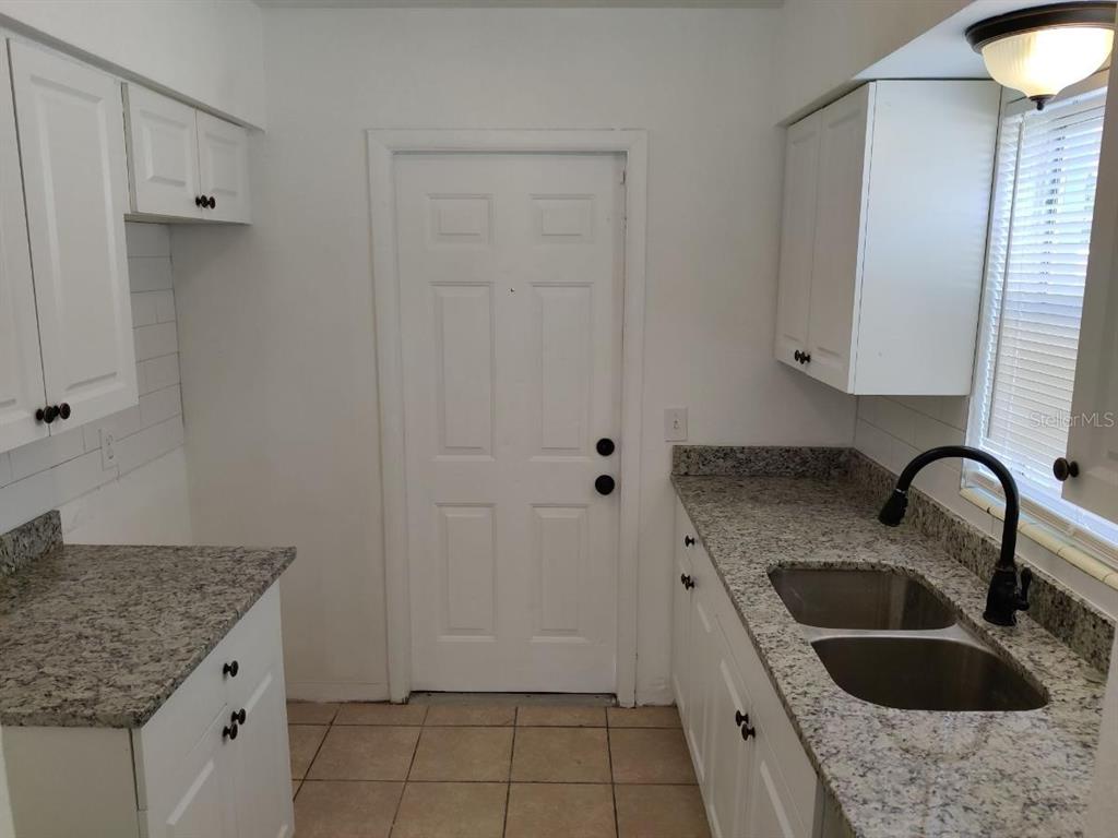 A kitchen features white cabinets, granite countertops, a double sink, and a white door — 245 - 247 38TH AVENUE SE, ST PETERSBURG, FL