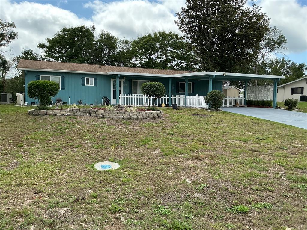 A teal single-story house features a white picket fence, a carport, and a stone planter — 10415 SW 99TH AVENUE, OCALA, FL