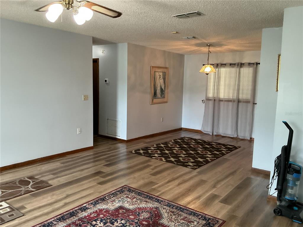 An open-concept living and dining area features wood-look flooring, ceiling fans, and area rugs — 10415 SW 99TH AVENUE, OCALA, FL