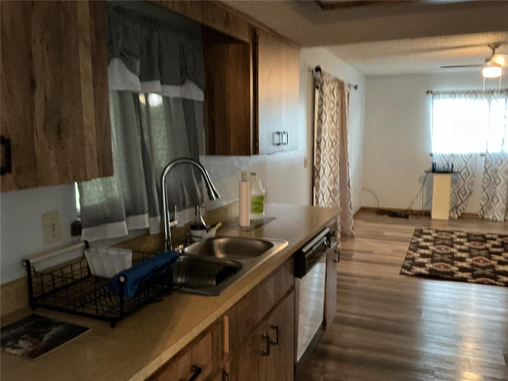 A kitchen with wood cabinets and a stainless steel sink overlooks a living area — 10415 SW 99TH AVENUE, OCALA, FL