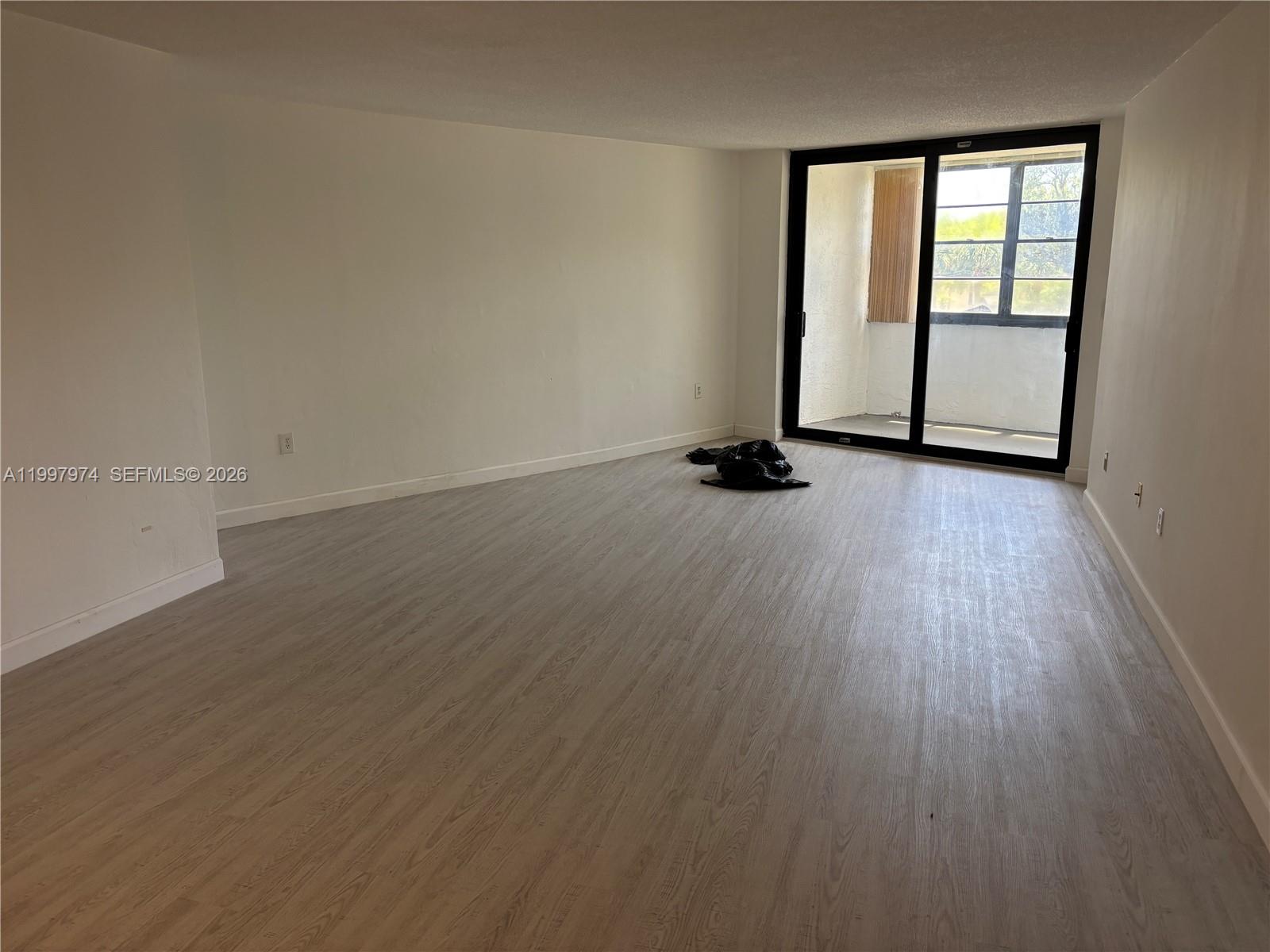 An empty room features light wood-look flooring, white walls, and a sliding glass balcony door — 10854 N KENDALL DR # 316, Miami FL 33176, MIAMI, FL