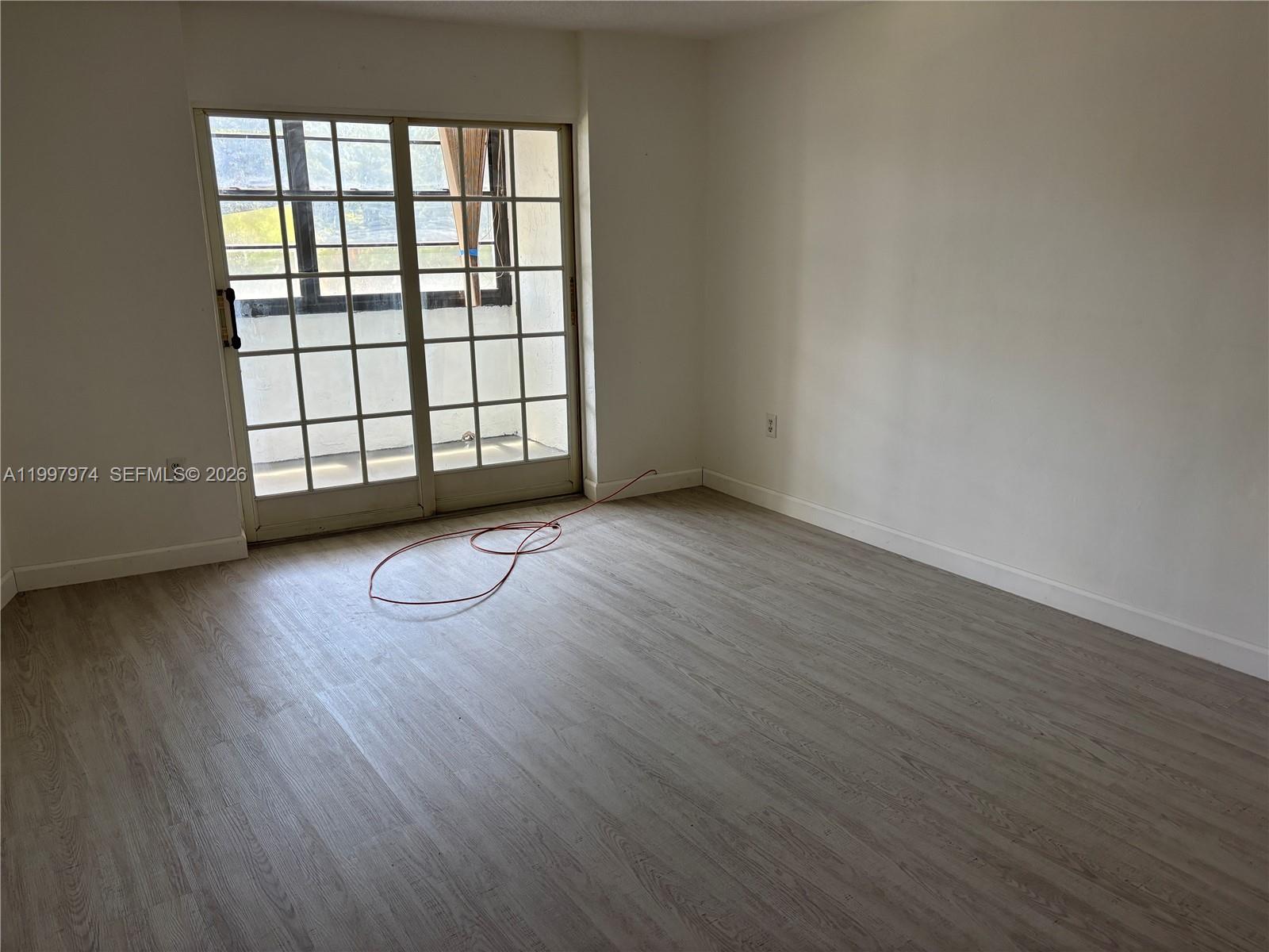 An empty room features light wood-look flooring, white walls, and a sliding glass door — 10854 N KENDALL DR # 316, Miami FL 33176, MIAMI, FL