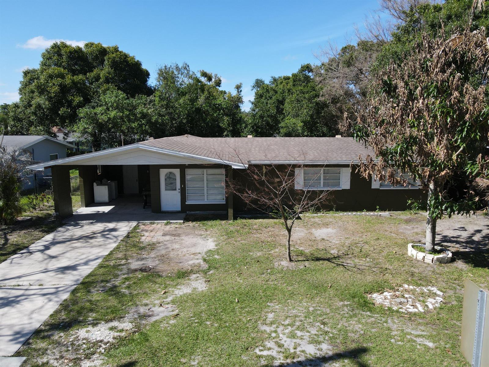 An exterior view of a single-story house with a carport, brown siding, and a front yard — 2110 Cortez Boulevard, Fort Pierce FL 34982, FORT PIERCE, FL