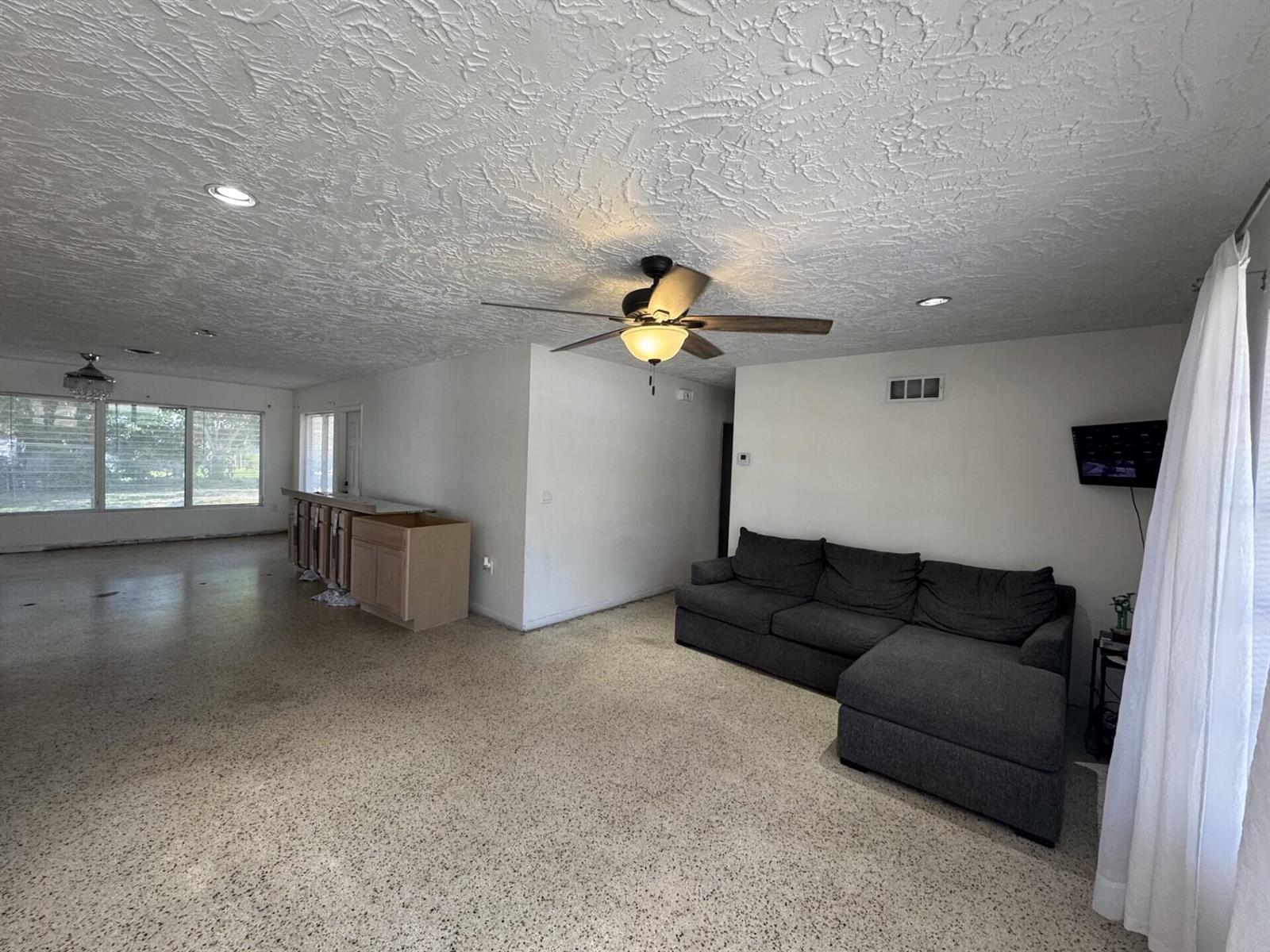 A living room with a gray sectional sofa, a ceiling fan, and speckled flooring — 2110 Cortez Boulevard, Fort Pierce FL 34982, FORT PIERCE, FL