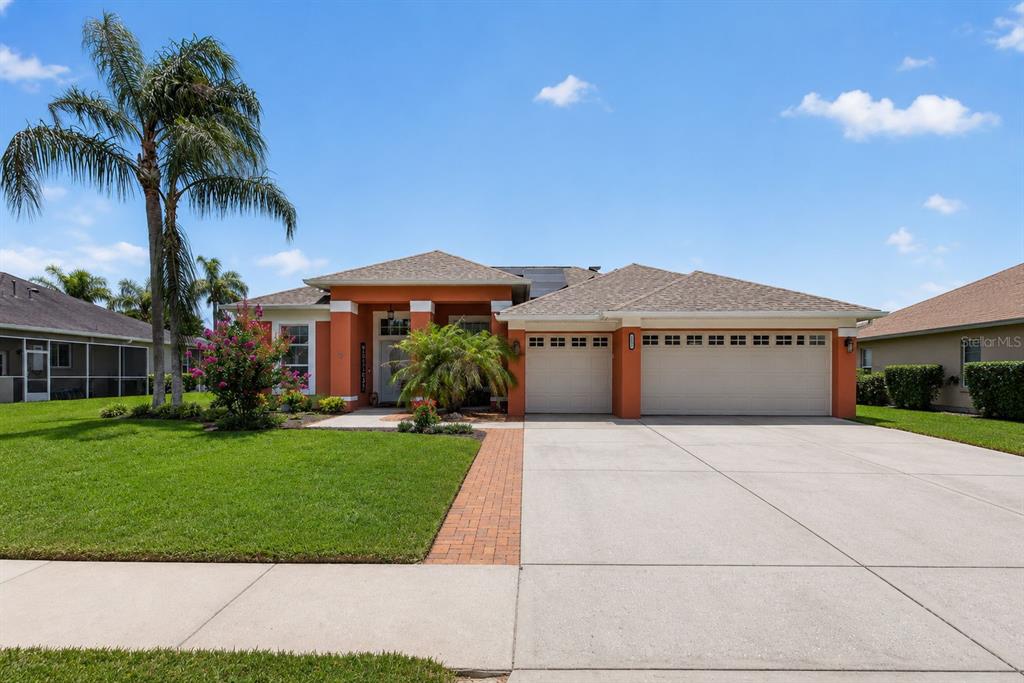 A single-story house with an orange exterior, a three-car garage, and a palm tree — 5805 WEDGEFIELD DRIVE, ZEPHYRHILLS, FL