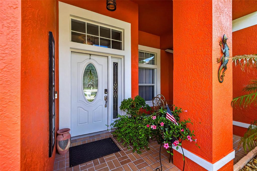 An orange-walled entryway features a white front door with a glass insert and a lizard — 5805 WEDGEFIELD DRIVE, ZEPHYRHILLS, FL