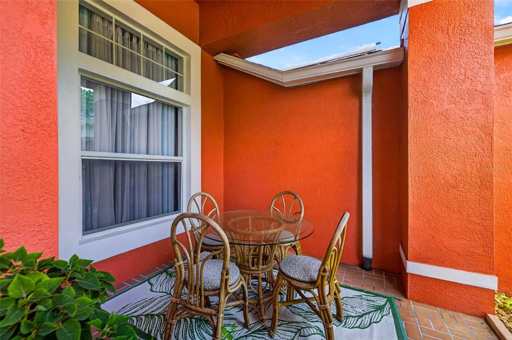 A small outdoor patio features a glass-topped table with four rattan chairs on a rug — 5805 WEDGEFIELD DRIVE, ZEPHYRHILLS, FL