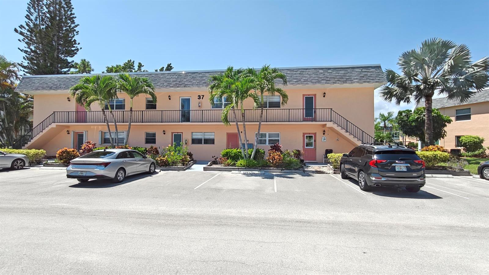 A two-story peach-colored apartment building with palm trees and parked cars in front — 2950 SE Ocean Boulevard # 6, Stuart FL 34996, STUART, FL
