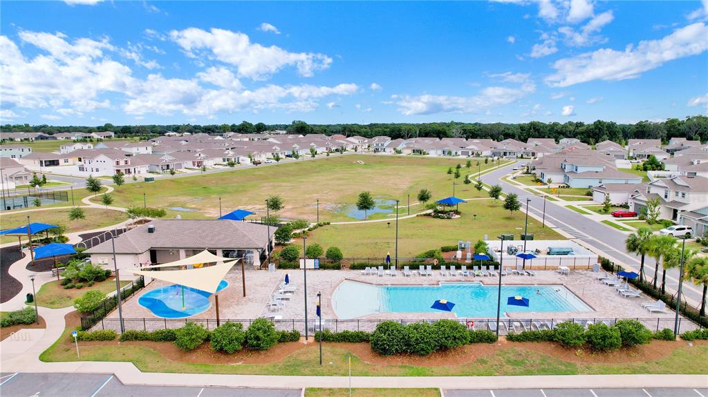 An aerial view shows a community swimming pool, splash pad, and clubhouse near residential homes — 7185 SW 63RD STREET, OCALA, FL