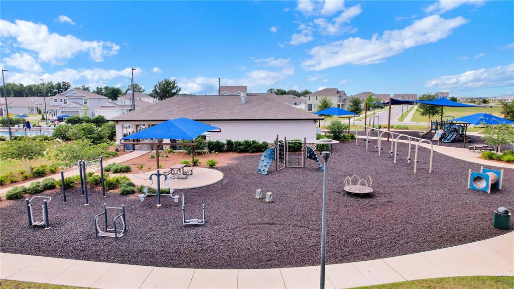 A playground with climbing structures, swings, and blue shade sails sits behind a community building — 7185 SW 63RD STREET, OCALA, FL
