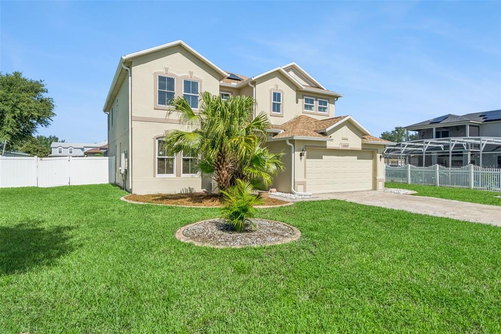 A two-story suburban house with a beige stucco exterior, a two-car garage, and palm trees — 15507 MARBLEHEAD WAY, CLERMONT, FL