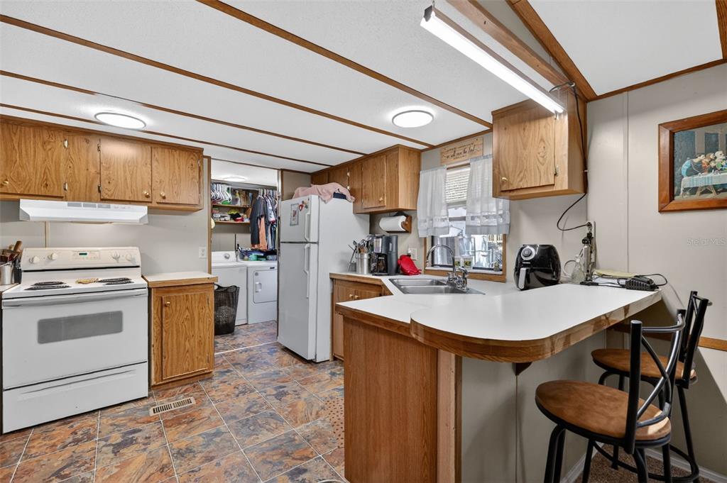 A kitchen with wood cabinets, white appliances, a breakfast bar, and a laundry area — 1710 INDIAN TRAIL UNIT B, LEESBURG, FL