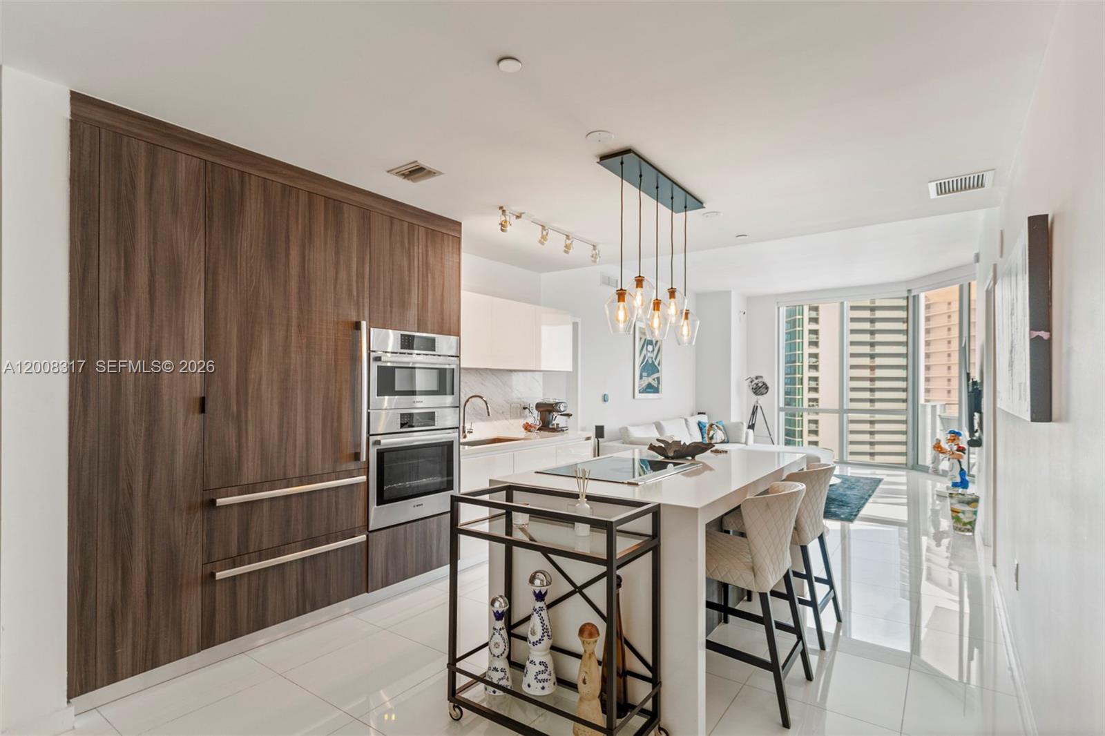 A modern kitchen features wood cabinetry, a white island with bar seating, and stainless appliances — 851 NE 1st Ave # 3707, Miami FL 33132, MIAMI, FL