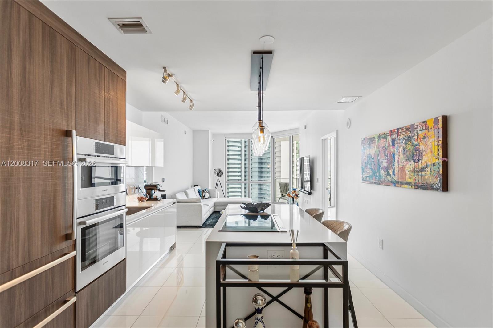 A modern kitchen features white cabinetry, a central island with a cooktop, and stainless appliances — 851 NE 1st Ave # 3707, Miami FL 33132, MIAMI, FL