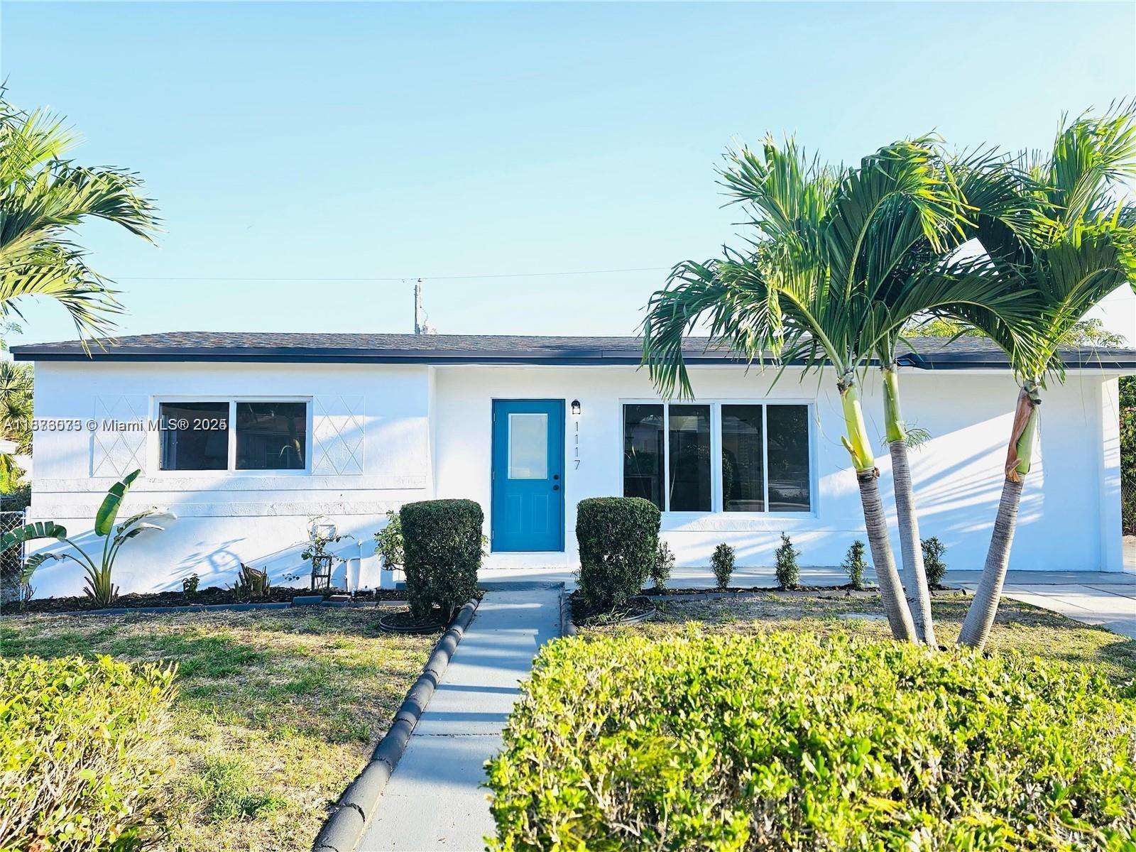 A single-story white house features a bright blue front door and two palm trees — 1117 W 26th Ct, Riviera Beach FL 33404, RIVIERA BEACH, FL