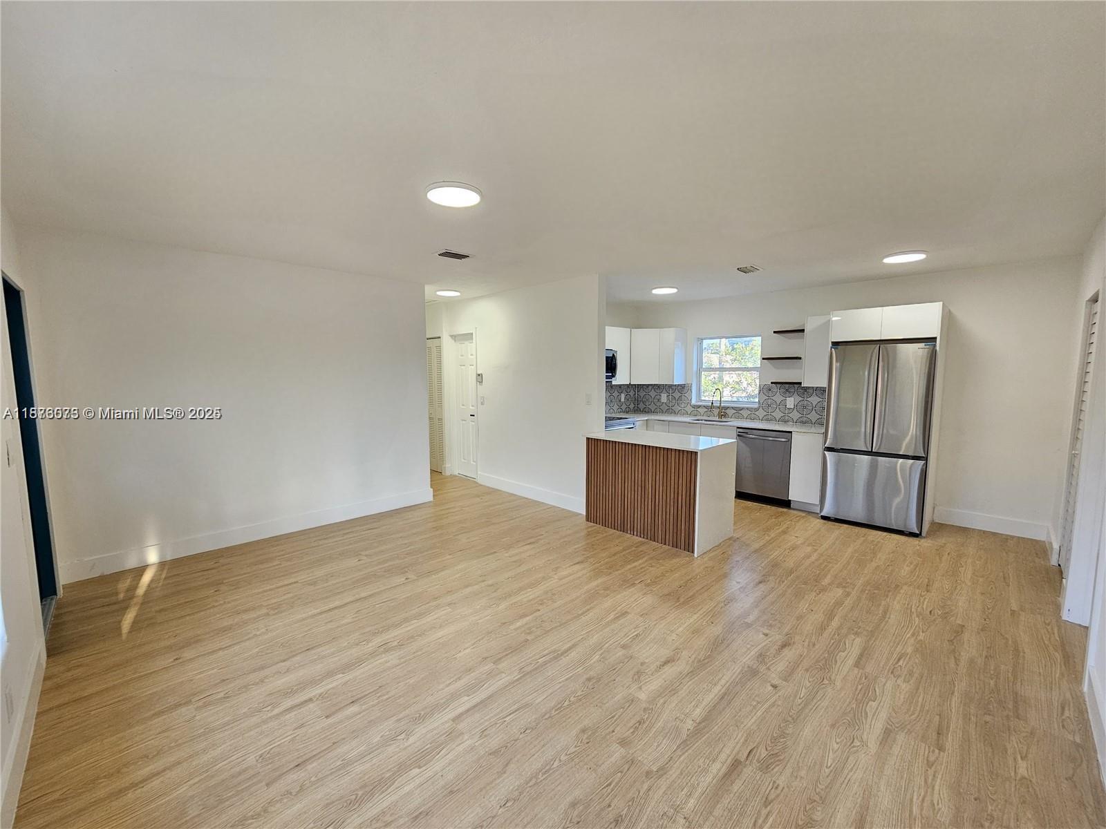 An open-concept kitchen with a wood-paneled island and stainless steel appliances overlooks a living area — 1117 W 26th Ct, Riviera Beach FL 33404, RIVIERA BEACH, FL