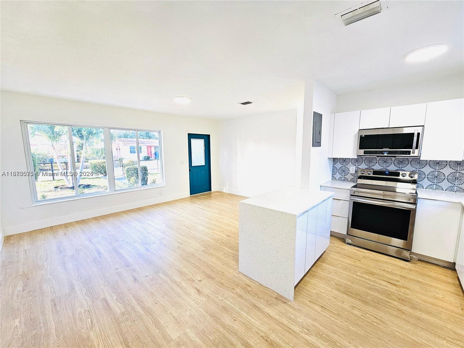 A kitchen with white cabinets and a small island opens into a living area — 1117 W 26th Ct, Riviera Beach FL 33404, RIVIERA BEACH, FL