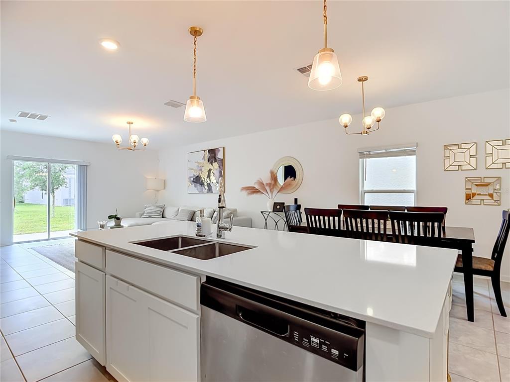 A kitchen island with a stainless steel dishwasher overlooks an open-concept living and dining area — 526 HATTERAS ROAD, DAVENPORT, FL