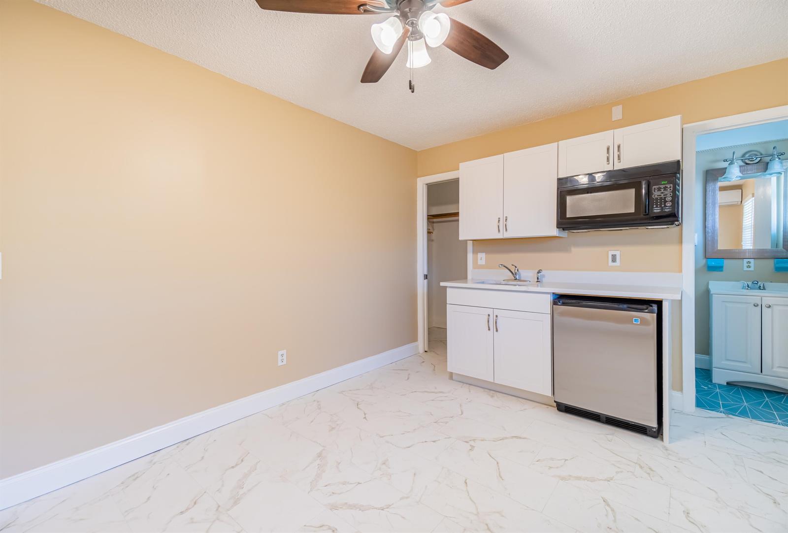 A kitchenette features white cabinets, a stainless steel mini-fridge, and marble-patterned tile flooring — 2546 NE Hickory Avenue, Jensen Beach FL 34957, JENSEN BEACH, FL