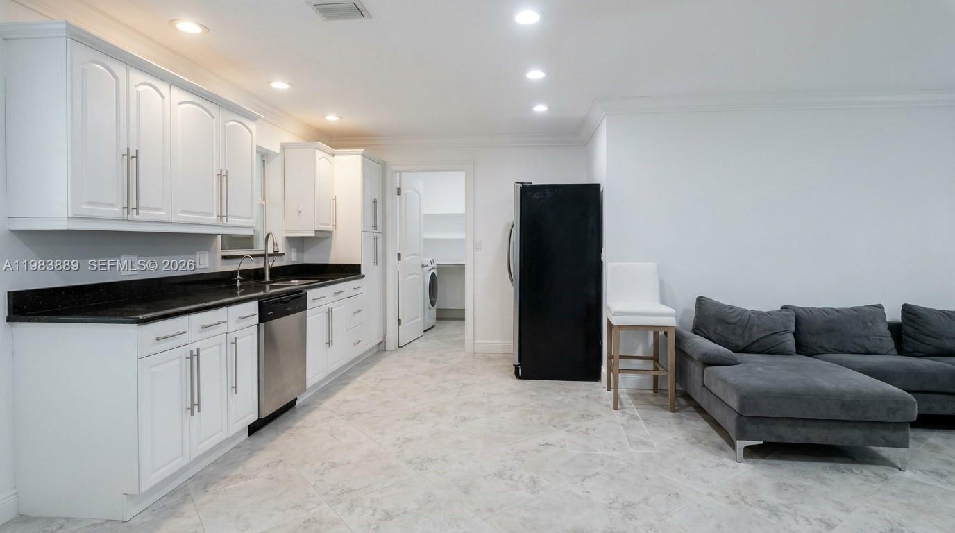 A kitchen with white cabinets, black countertops, and a stainless steel dishwasher next to a sofa — 804 NE 2nd St, Hallandale Beach FL 33009, HALLANDALE BEACH, FL