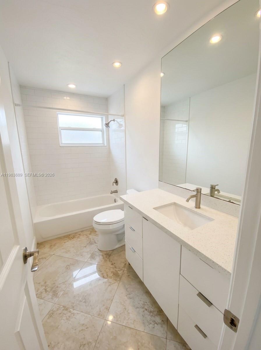 A bathroom features a white vanity, a tiled bathtub shower combo, and marble-look flooring — 804 NE 2nd St, Hallandale Beach FL 33009, HALLANDALE BEACH, FL