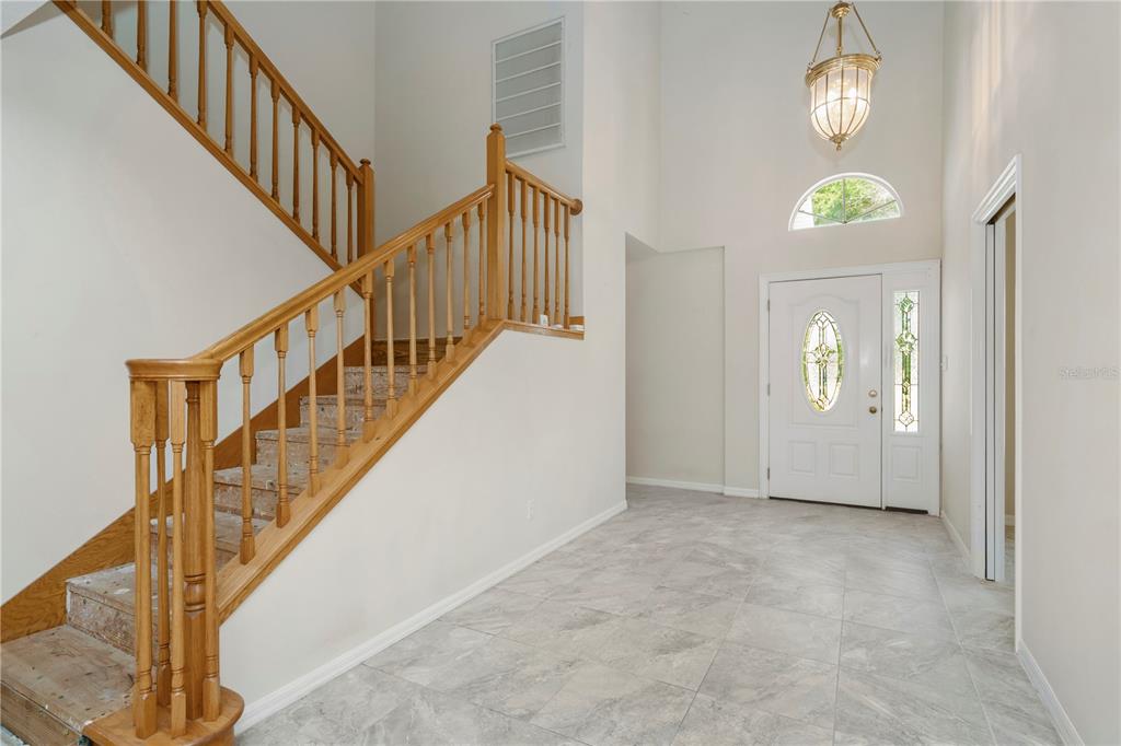 A foyer with light gray tile flooring, a wooden staircase, and a white front door — 785 DUQUE ROAD, LUTZ, FL