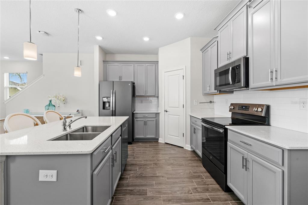 A modern kitchen features gray cabinets, white countertops, a central island, and stainless steel appliances — 17167 WRITING ALLEY, WINTER GARDEN, FL