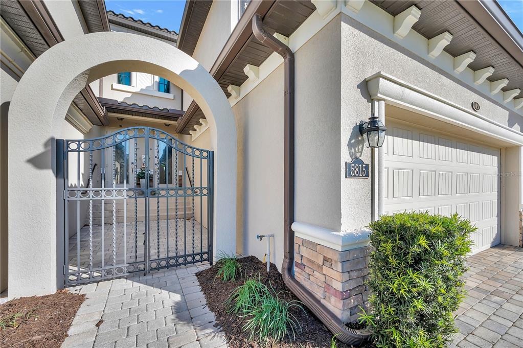 A gated courtyard entrance leads to a house with a stone-accented garage and stucco exterior — 5815 WAKE FOREST RUN UNIT 103, LAKEWOOD RANCH, FL