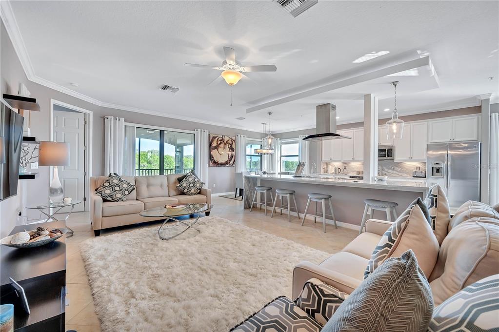 An open-concept living room and kitchen featuring a large rug, sectional sofa, and island seating — 5815 WAKE FOREST RUN UNIT 103, LAKEWOOD RANCH, FL