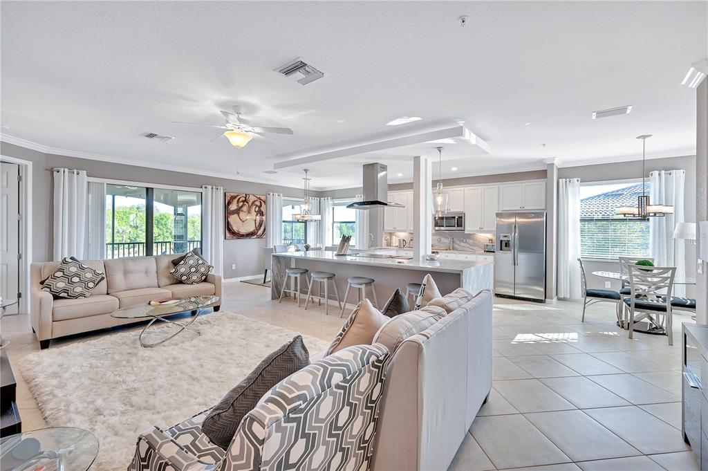 An open-concept living room and kitchen featuring a large island, tile floors, and neutral furniture — 5815 WAKE FOREST RUN UNIT 103, LAKEWOOD RANCH, FL