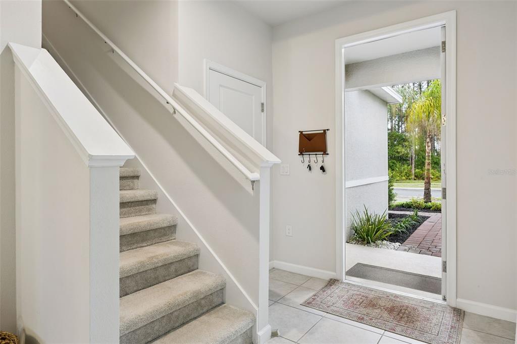 An entryway features a carpeted staircase, tiled flooring, a wall-mounted key rack, and an open door — 1472 EUCALYPTUS WAY, DAVENPORT, FL
