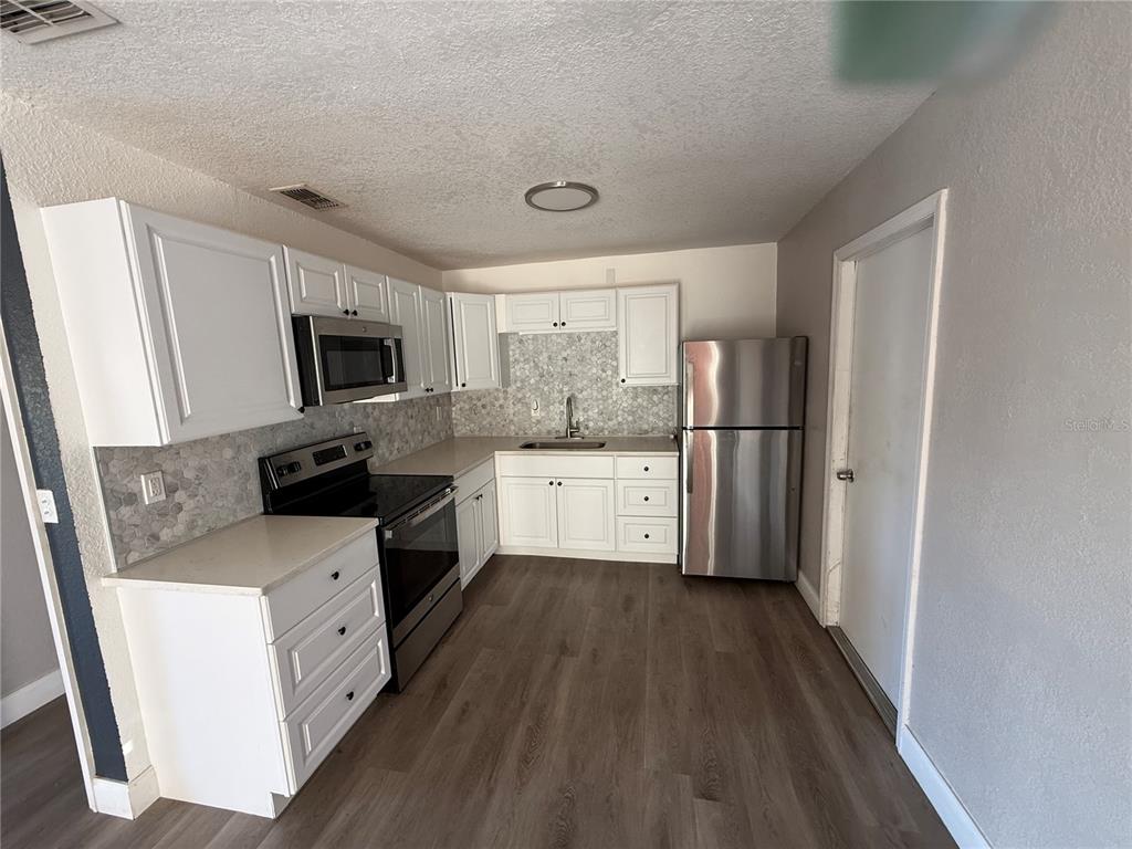 A kitchen features white cabinets, stainless steel appliances, a tiled backsplash, and wood-look flooring — 1611 FRUITWOOD DRIVE, LAKELAND, FL