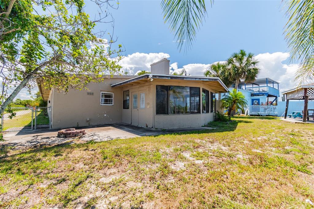 The exterior of a tan house features a glass-enclosed sunroom and a concrete patio area — 5325 TREADWAY DRIVE, PORT RICHEY, FL