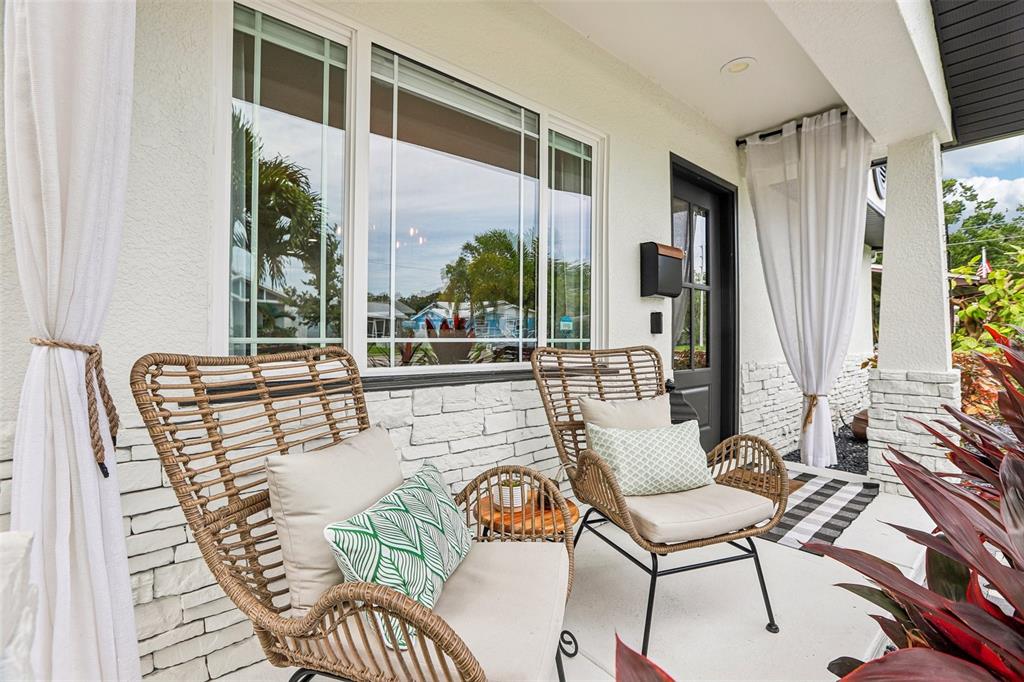 A covered porch features two wicker chairs, white curtains, and a stone-veneer exterior wall — 472 36TH AVENUE N, ST PETERSBURG, FL