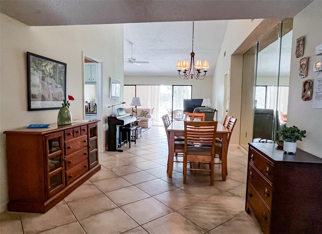 A dining area with a wooden table and chairs sits adjacent to a living room — 690 BIRD BAY CIRCLE UNIT 28, VENICE, FL