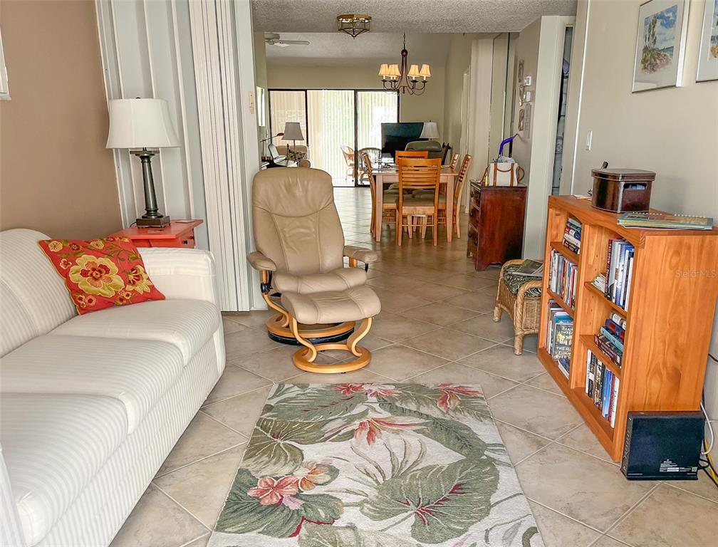 A living room with tile floors, a white sofa, a recliner, and a wooden bookshelf — 690 BIRD BAY CIRCLE UNIT 28, VENICE, FL