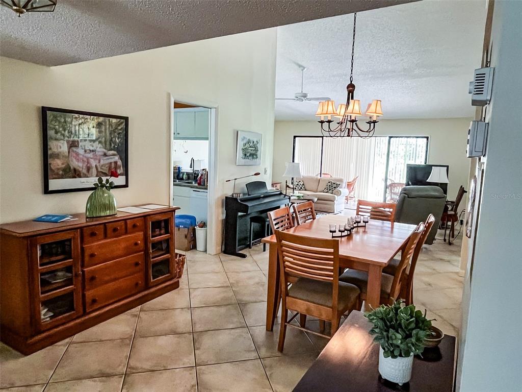 A dining area with a wooden table and chairs sits adjacent to a living room — 690 BIRD BAY CIRCLE UNIT 28, VENICE, FL