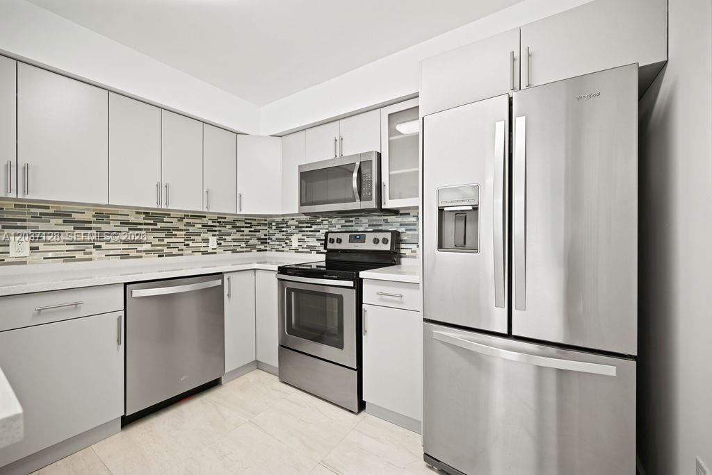 A modern kitchen features stainless steel appliances, white cabinetry, and a patterned tile backsplash — 4420 NW 107th Ave # 107, Doral FL 33178, DORAL, FL