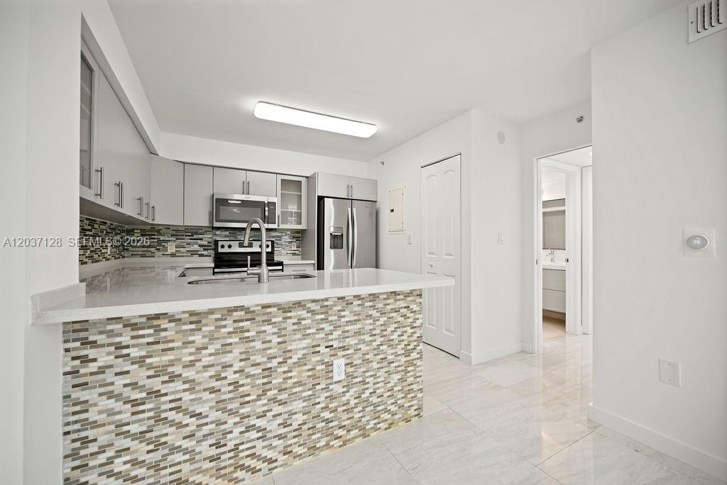 A modern kitchen features a tiled breakfast bar, stainless steel appliances, and white cabinetry — 4420 NW 107th Ave # 107, Doral FL 33178, DORAL, FL