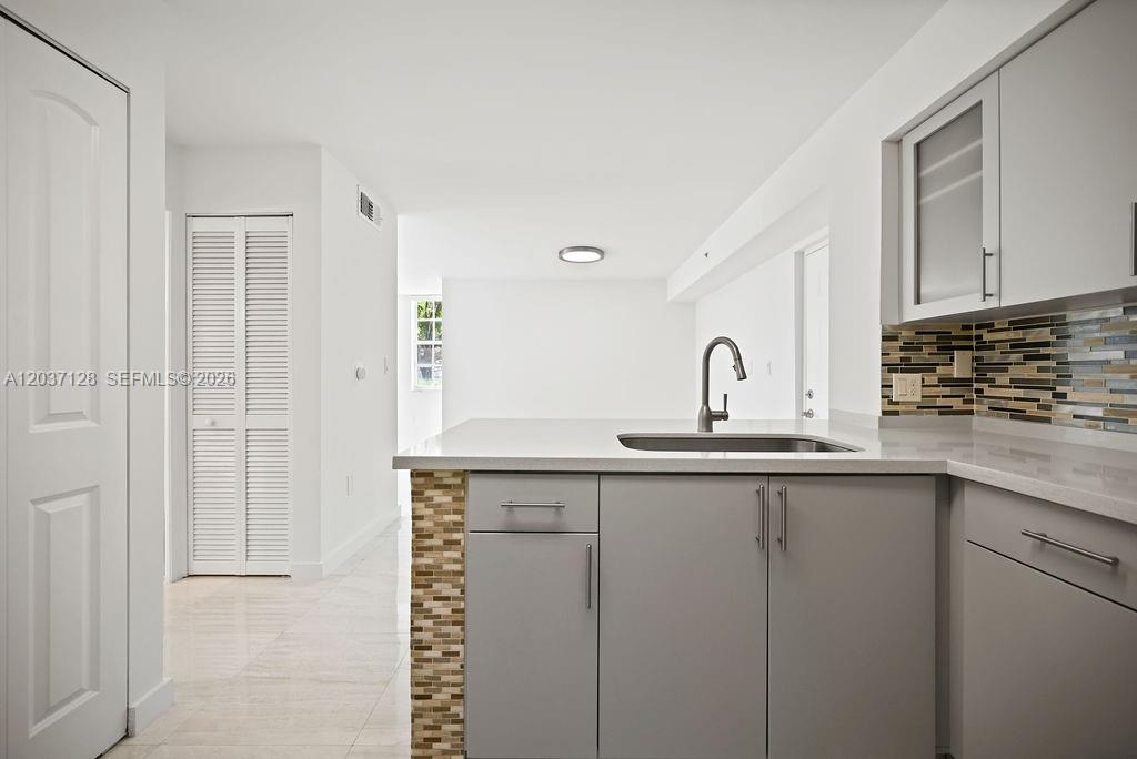 A kitchen features gray cabinets, a light countertop, and a mosaic tile backsplash — 4420 NW 107th Ave # 107, Doral FL 33178, DORAL, FL