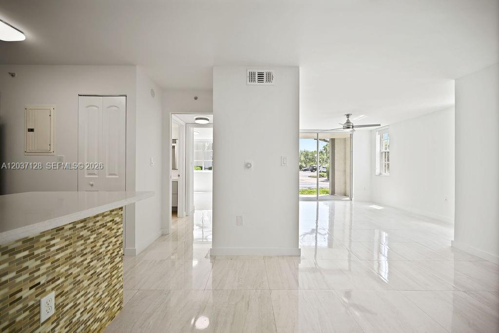 A bright, open-concept living area features white tile flooring, a kitchen peninsula, and sliding glass doors — 4420 NW 107th Ave # 107, Doral FL 33178, DORAL, FL