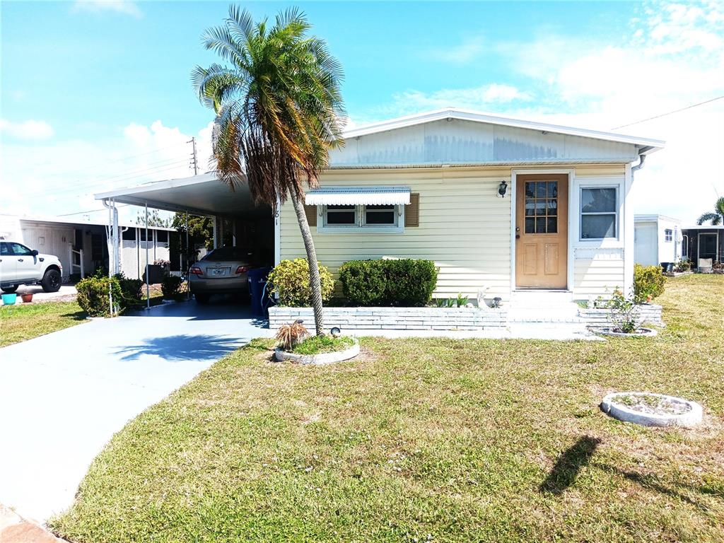 A single-story mobile home with light yellow siding, a carport, and a palm tree — 1781 OLYMPIA FIELDS STREET, SARASOTA, FL